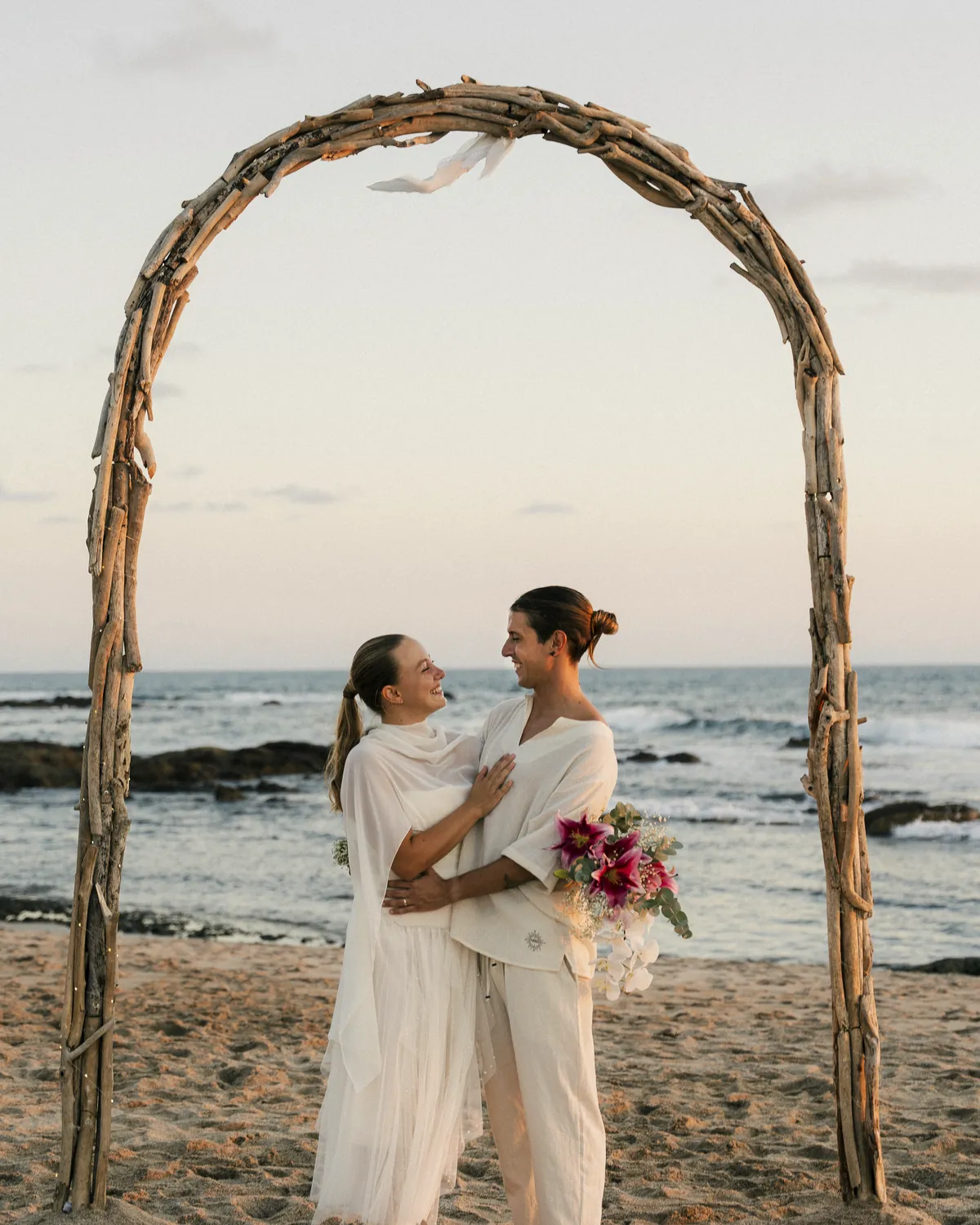 Pareja bajo un portal de madera de mar en la playa al atardecer